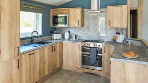 A kitchen with wooden cabinets, a stainless steel stove, a microwave, and a sink. - Exclusive 2 bedroom Sauna Lodge sleeps 4 (Landford, Nr Salisbury)