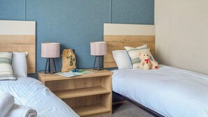 A hotel room with two beds, a wooden nightstand, two lamps, a teddy bear, and a bag with text. - Exclusive 2 bedroom Sauna Lodge sleeps 4 (Landford, Nr Salisbury)