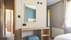 Une chambre d’hôtel avec un bureau en bois, un miroir, deux lits, un pouf bleu et un radiateur.