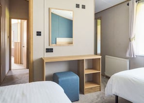 A hotel room with a wooden desk, a mirror, two beds, a blue ottoman, and a radiator. - Exclusive 2 bedroom Sauna Lodge sleeps 4 (Landford, Nr Salisbury)