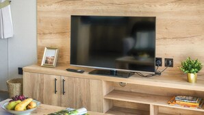 A modern living room with a flat-screen TV, wooden entertainment unit, a bowl of fruit, magazines, and a potted plant. - Exclusive 2 bedroom Sauna Lodge sleeps 4 (Landford, Nr Salisbury)