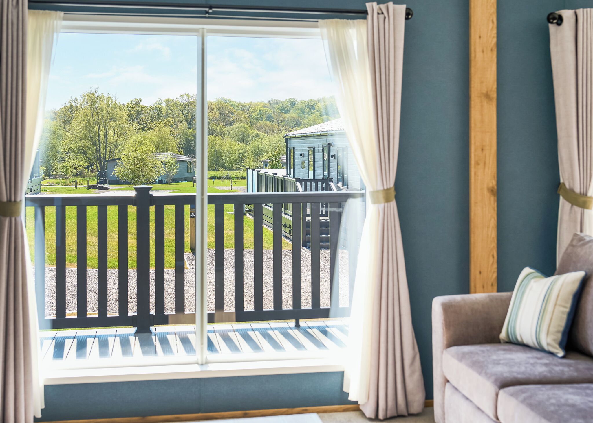 Une pièce avec vue sur un paysage verdoyant, un balcon doté d’une balustrade et un canapé agrémenté d’un coussin.