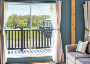 A room with a view of a green landscape, a balcony with a railing, and a couch with a cushion.