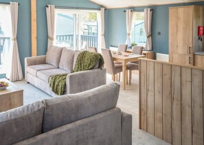 A cozy living area with a sofa, a dining table, and a wooden cabinet. - Exclusive 2 bedroom Sauna Lodge sleeps 4 (Landford, Nr Salisbury)