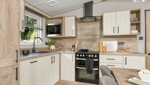 Eine moderne Küche mit integriertem Kochfeld, Backofen und Mikrowelle, Holzschränken und einem Fenster mit Jalousien.