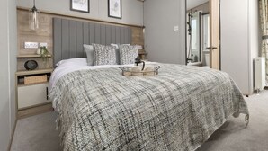 Ein Schlafzimmer mit einem Bett, Nachttischen, einem Wandregal, einem gerahmten Bild und einer Tür zu einem anderen Raum.