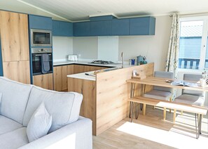 A modern kitchen with blue cabinets, a built-in oven, and a dining area with a bench and table. - Exclusive 2 bedroom Lodge sleeps 4 (Pet) (Landford, Nr Salisbury)