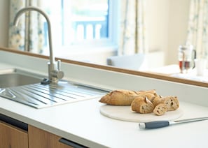 Una cocina con un lavamanos de acero inoxidable, una tabla de cortar con pan y un cuchillo.