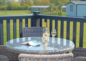 Een ronde glazen tafel met rieten stoelen op een balkon, een fles en twee wijnglazen.