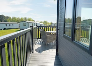Een balkon met rieten stoelen en een tafel, met uitzicht op een grasveld met stacaravans.