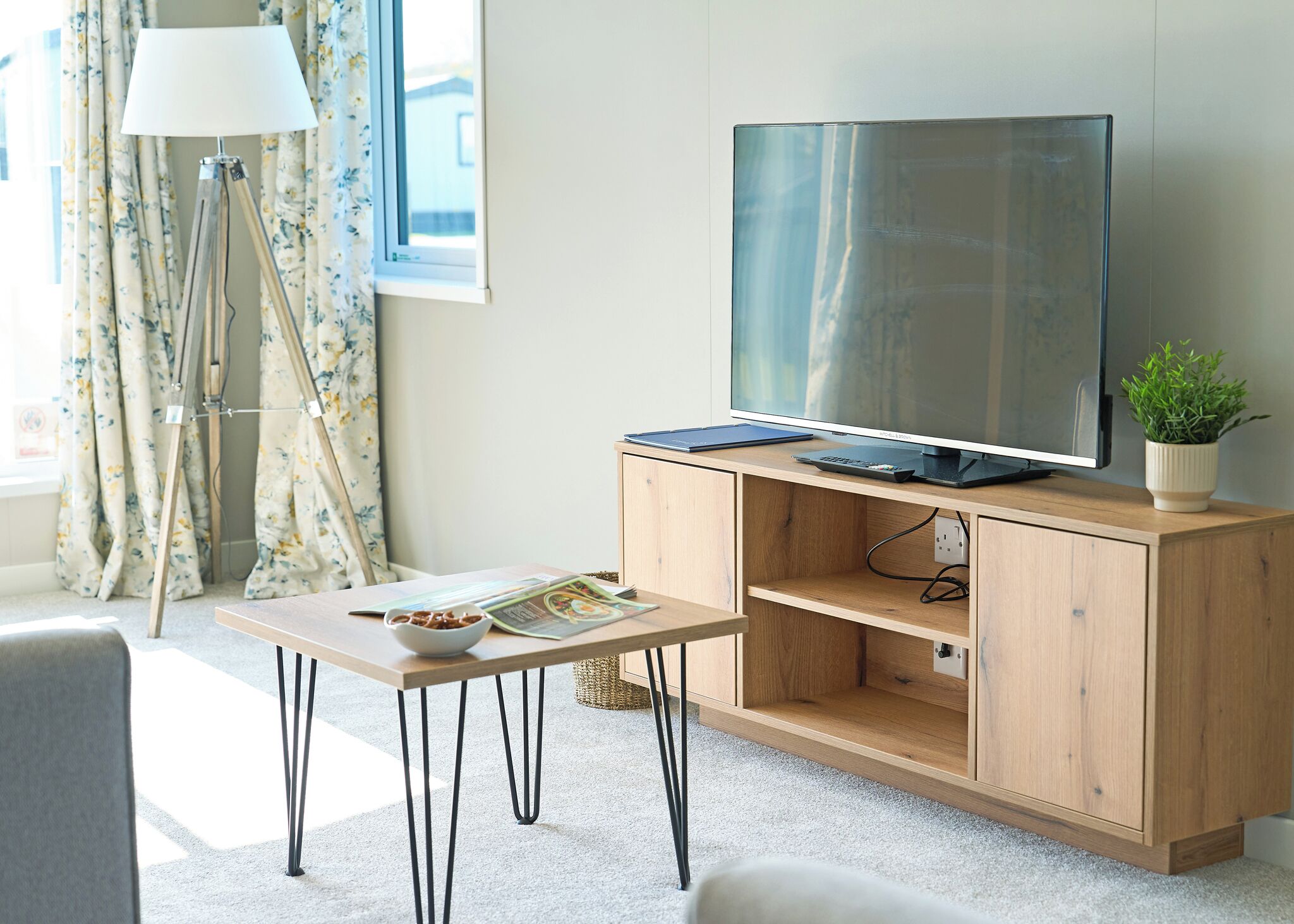 A modern living room with a flat-screen TV, wooden cabinet, and a small table with a bowl and magazine.