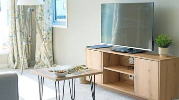 A modern living room with a flat-screen TV, wooden cabinet, and a small table with a bowl and magazine.