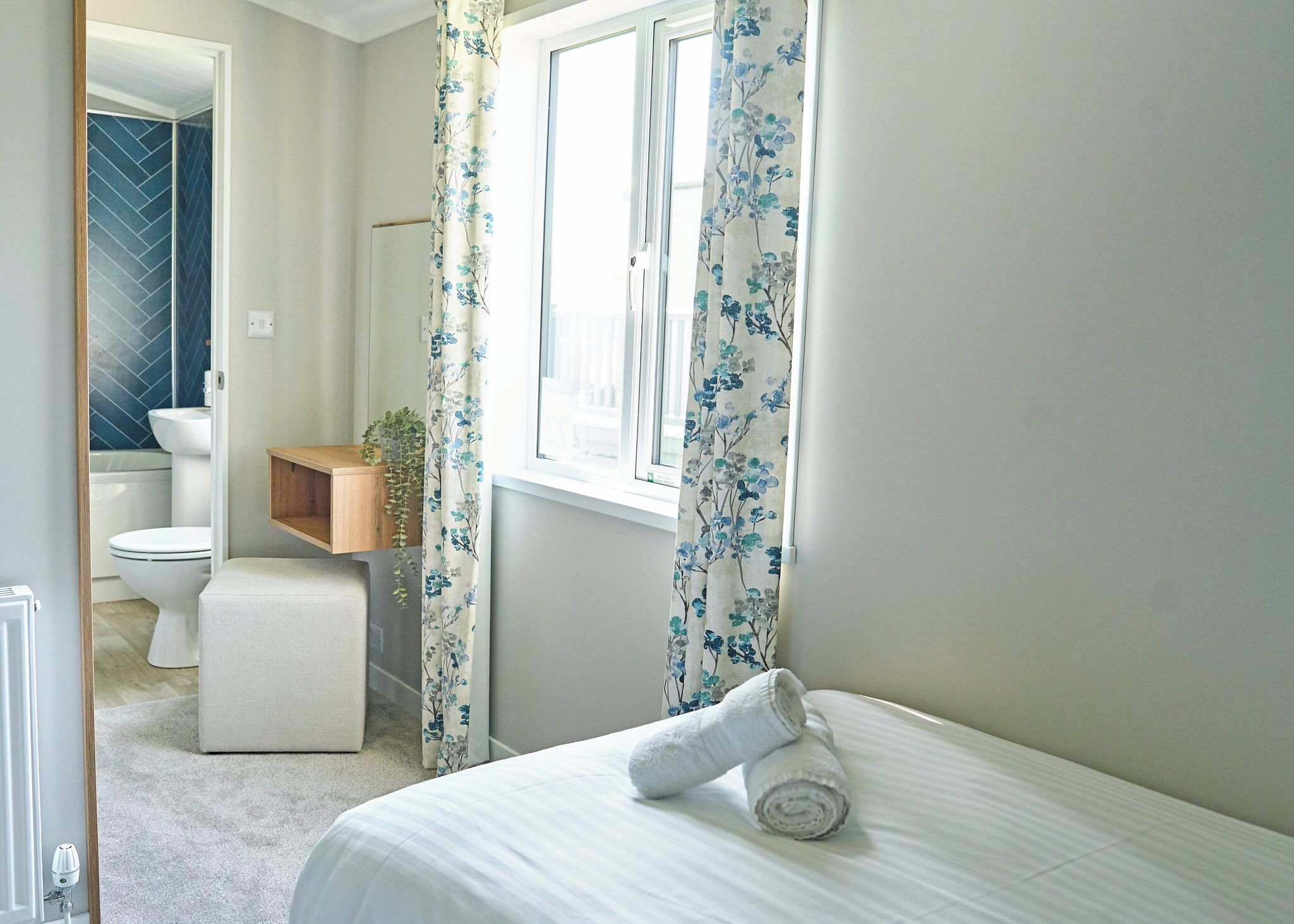 A bedroom with a bed, a window with curtains, a bedside table, and a view of the bathroom.