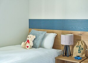 A bed with a white sheet, a teddy bear, a lamp, a small bag, and a pair of binoculars on a wooden nightstand. - Exclusive 2 bedroom Lodge sleeps 4 (Pet) (Landford, Nr Salisbury)