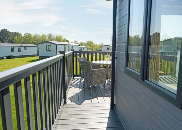A balcony with wicker chairs and a table, overlooking a grassy area with mobile homes. - Exclusive 2 bedroom Lodge sleeps 4 (Pet) (Landford, Nr Salisbury)
