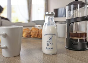 Eine weiße Tasse, eine Flasche frische Milch vom Bauernhof und eine Kaffeemaschine auf einem Holztisch.