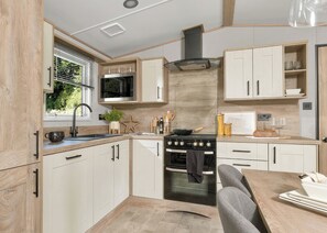 Eine moderne Küche mit integriertem Kochfeld, Backofen und Mikrowelle, Holzschränken und einem Fenster mit Jalousien.