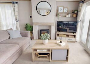 Ein modernes Wohnzimmer mit Sofa, Couchtisch, Kamin, Fernseher und einem großen Fenster.