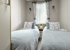 A bedroom with two beds, a nightstand with a vase, and a window with curtains. - Premium Hot Tub 2 bedroom Holiday Home sleeps 6 (Hayle)