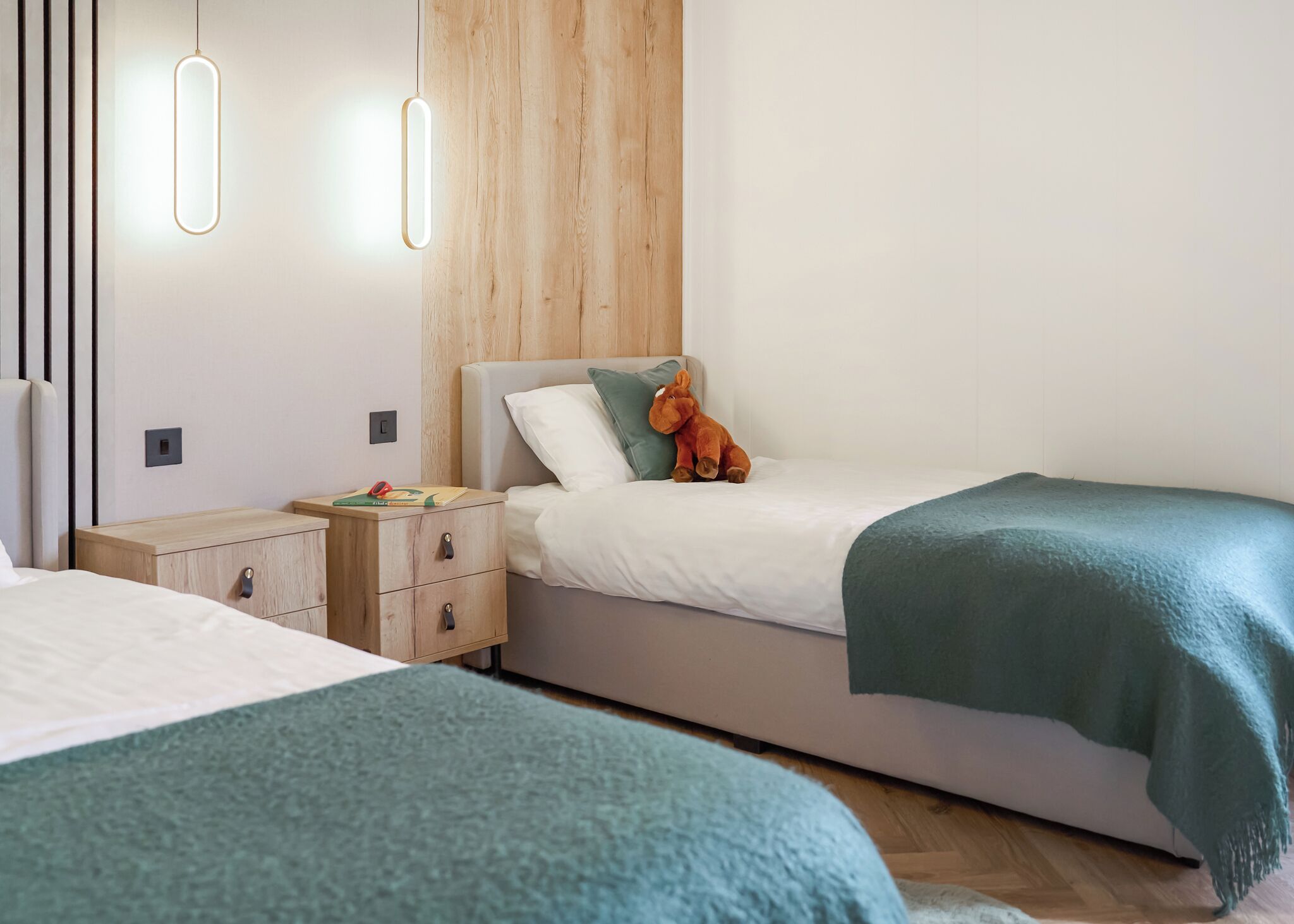 Ein modernes Schlafzimmer mit zwei Betten, einem Holzkopfende, Nachttischen und einer hängenden Leuchte.
