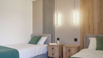 A modern hotel room with two single beds, a nightstand with a lamp, a wooden panel wall, and a ceiling light fixture.