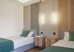 A modern hotel room with two single beds, a nightstand with a lamp, a wooden panel wall, and a ceiling light fixture.