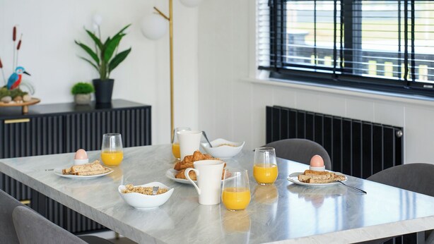 A breakfast table with croissants, orange juice, and a bowl of cereal. - Autograph Kos Hot Tub 2-bedroom Luxury Lodge slp 4 (Landford, Nr Salisbury)