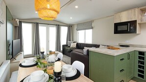 Een moderne keuken met een magnetron, groene kastjes en een eethoek met een tafel gedekt voor twee personen.
