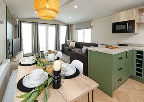 A modern kitchen with a microwave, green cabinets, and a dining area with a table set for two. - A stylish and contemporary retreat designed with comfort and quality in mind. (Peterborough)