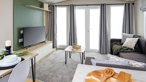 Een moderne woonkamer met een flatscreen televisie, een eettafel en een bank met kussens.