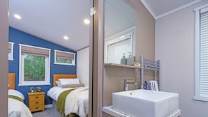Ein Schlafzimmer mit zwei Betten, einem Badezimmer mit Waschbecken und einem Fenster mit Jalousien.