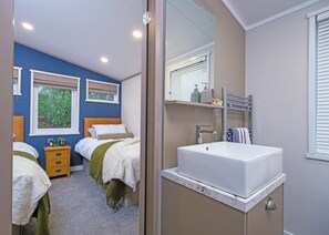 Ein Schlafzimmer mit zwei Betten, einem Badezimmer mit Waschbecken und einem Fenster mit Jalousien.