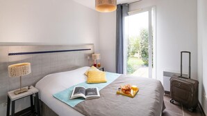 Ein Hotelzimmer mit Bett, Nachttisch mit Lampe, Koffer und Fenster mit Blick auf Grünfläche.