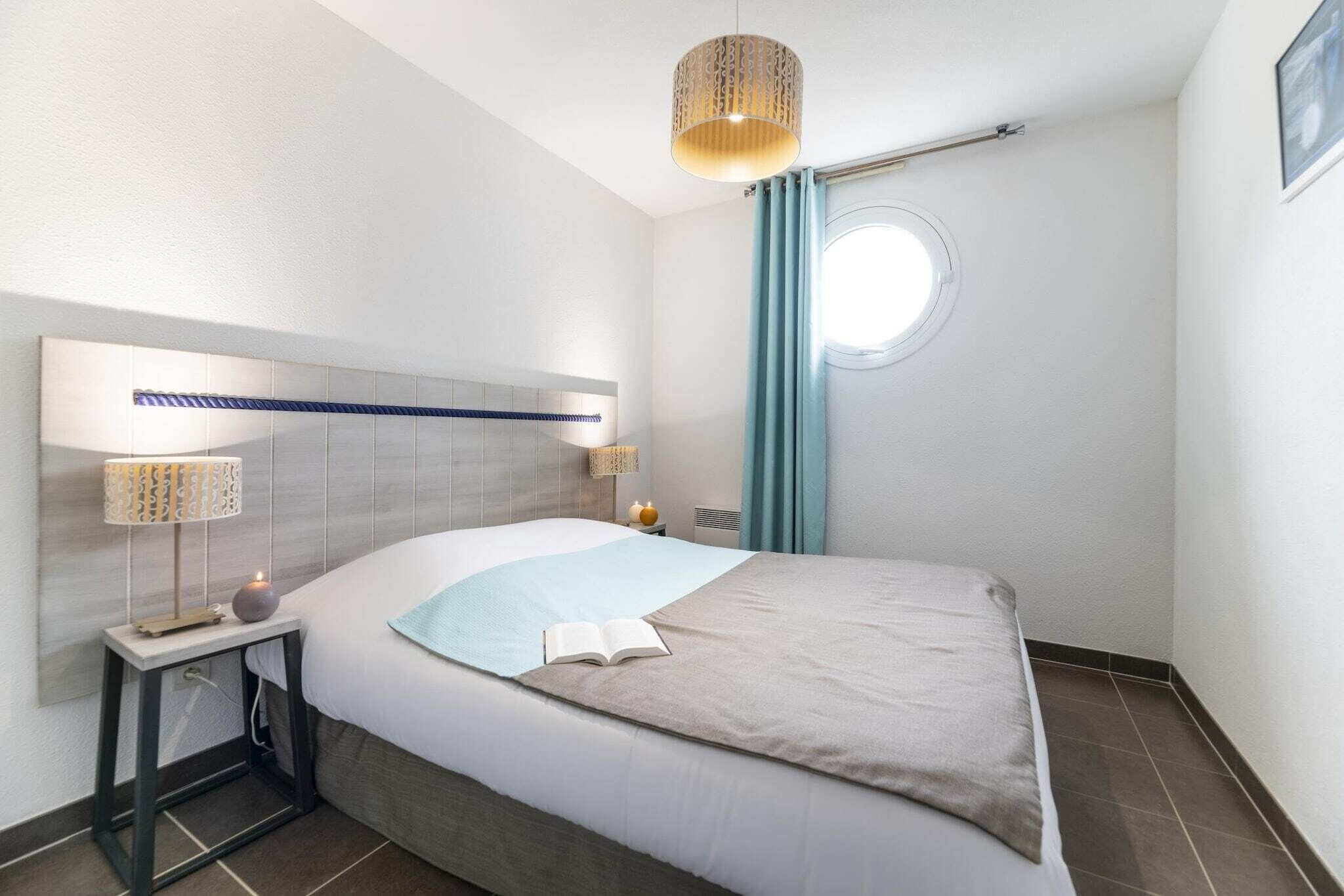 A modern hotel room with a large bed, bedside lamps, a window with curtains, and a ceiling light fixture.