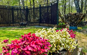 A fenced garden area with a fire pit, a pile of firewood, and flowering plants. - 2 bedroom stunning home in Hadsund (Hadsund)