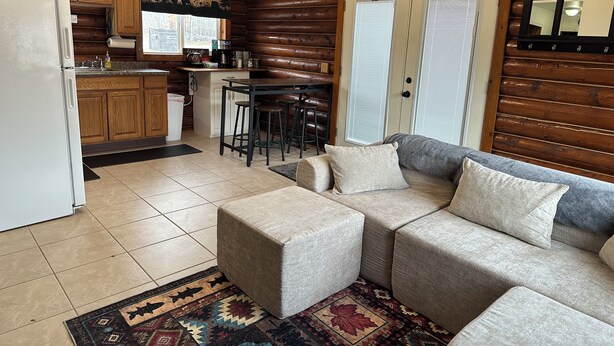 A log cabin interior with a kitchen, dining area, and a sofa with ottomans.