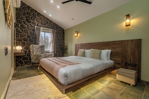Ein Schlafzimmer mit Steinwand, hölzernem Bettgestell, einem Nachttisch, einem Fenster mit Vorhängen und einem Deckenventilator.