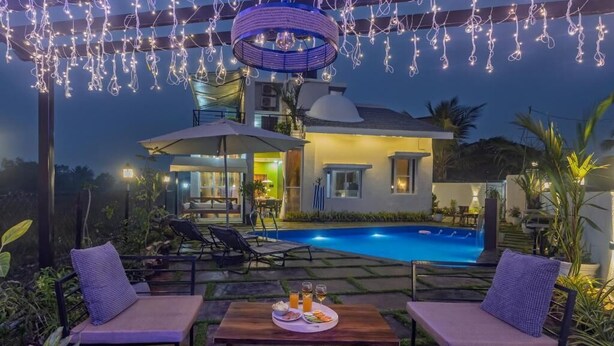 A poolside area with lounge chairs, a dining table with food and drinks, and a swimming pool. - ELIVAAS Moonlit retreat 3 BHK with Pool (Alibag)