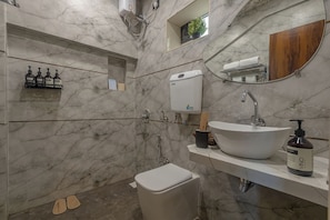 Ein Badezimmer mit Marmorwand, Toilette, Waschbecken mit Spiegel und Ablage für Toilettenartikel.