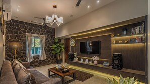 A modern living room with a stone wall, a sofa, a coffee table, a TV, a bookshelf, and a speaker. - ELIVAAS Moonlit retreat 3 BHK with Pool (Alibag)