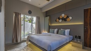 A modern bedroom with a large bed, a ceiling fan, a wall-mounted clock, and a decorative wall piece. - ELIVAAS Moonlit retreat 3 BHK with Pool (Alibag)