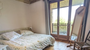 Un dormitorio con cama, piso de madera, una silla y un balcón con vistas.