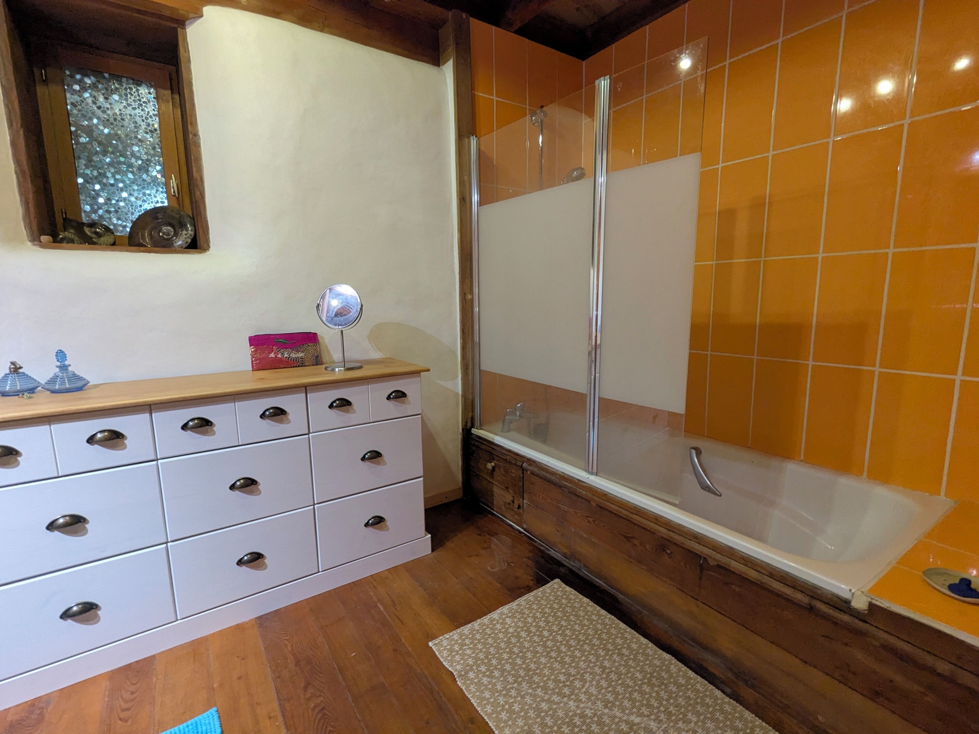 A bathroom with a wooden vanity, a glass shower enclosure, and a tiled wall.