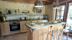 Una cocina con armarios de madera, una isla central con taburetes, un horno empotrado y varios utensilios de cocina en la pared.