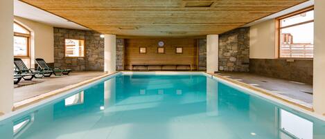 Ein Hallenbad mit Holzboden und Steinwänden, umgeben von Liegestühlen.