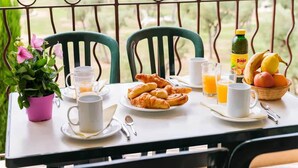 Una mesa de desayuno con croissants, jugo y una cesta de frutas en un balcón con vistas.