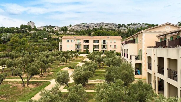 Un edificio con varios balcones, un patio con árboles y montañas al fondo.