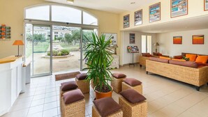 Habitación amplia con un gran ventanal que da a un patio, mobiliario de mimbre y una planta en maceta.