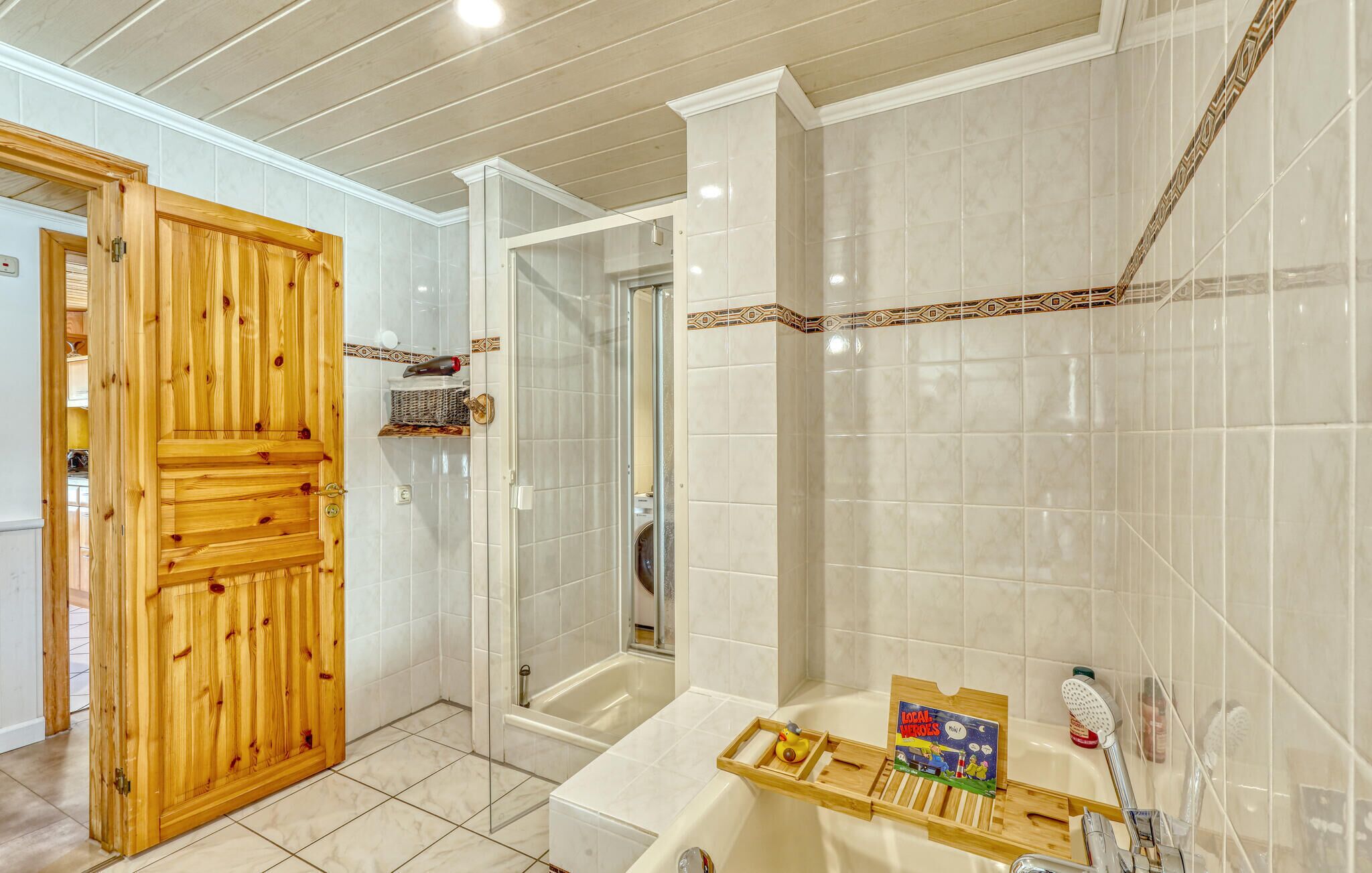 A bathroom with a wooden door, a shower, a bathtub, and a shelf with a book and a toy.