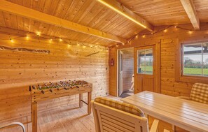 Een knus houten vertrek met een tafelvoetbaltafel, een tafel met stoelen en een raam met uitzicht op de omgeving.
